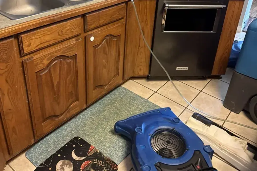 Air mover drying a kitchen floor in front of cabinets after an appliance leak in Canoga Park